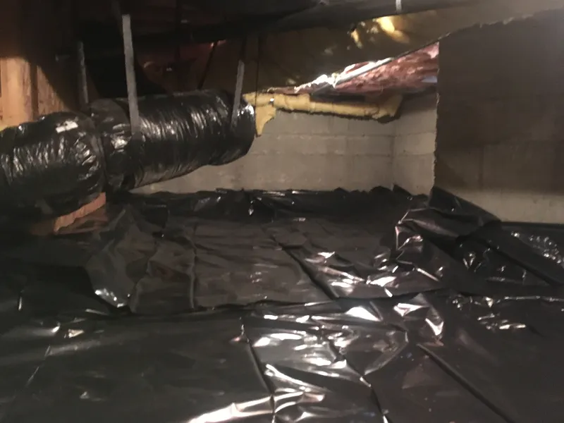 A crawl space area with new black plastic vapor barrier