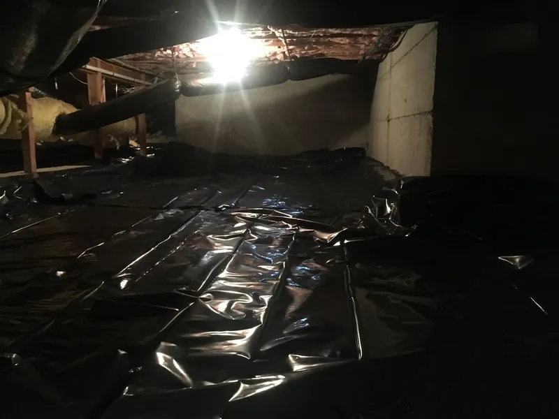 A crawl space area with black plastic sheeting covering the ground