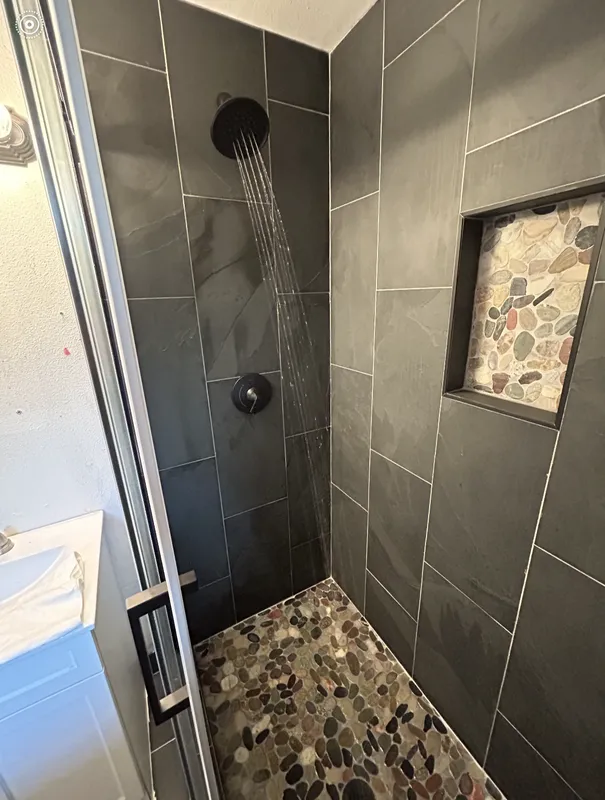 Black tile shower with stone floors and soap shelf